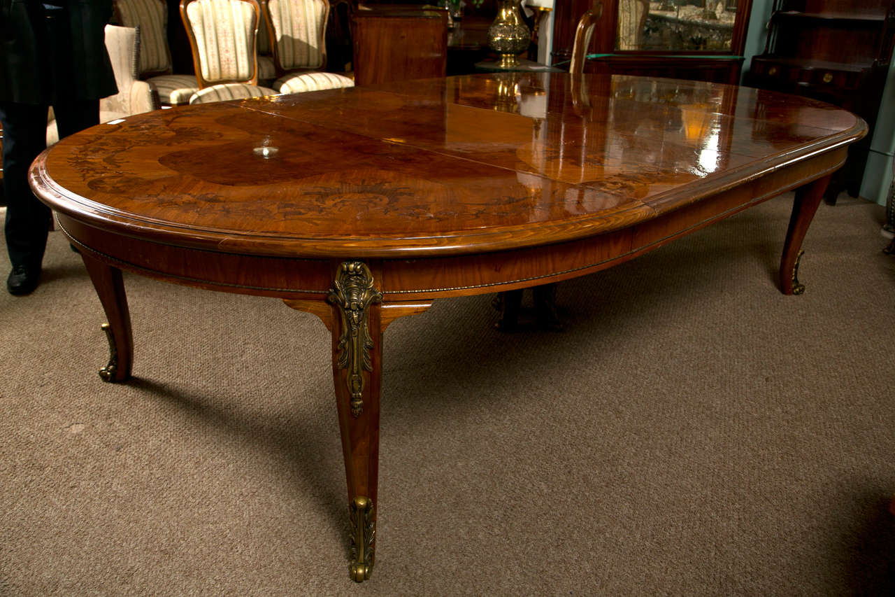A phenomenal mahogany oval dining table in the taste of French Louis XV, from the 2nd quarter of 20th century, the molded top with beautiful marquetry pattern of floral and foliage, atop a frieze decorated with bronze beaded banding, raised on