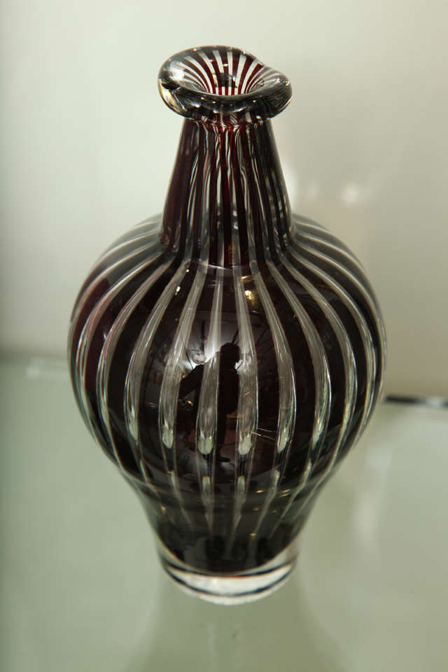 Orrefors Ariel vase by Edvin Öhrström, Sweden, 20th century.
Thick-walled bottle form with raised asymmetrical rim on a colorless body internally decorated with vertical aubergine stripes, inscribed on base Orrefors Ariel Sweden