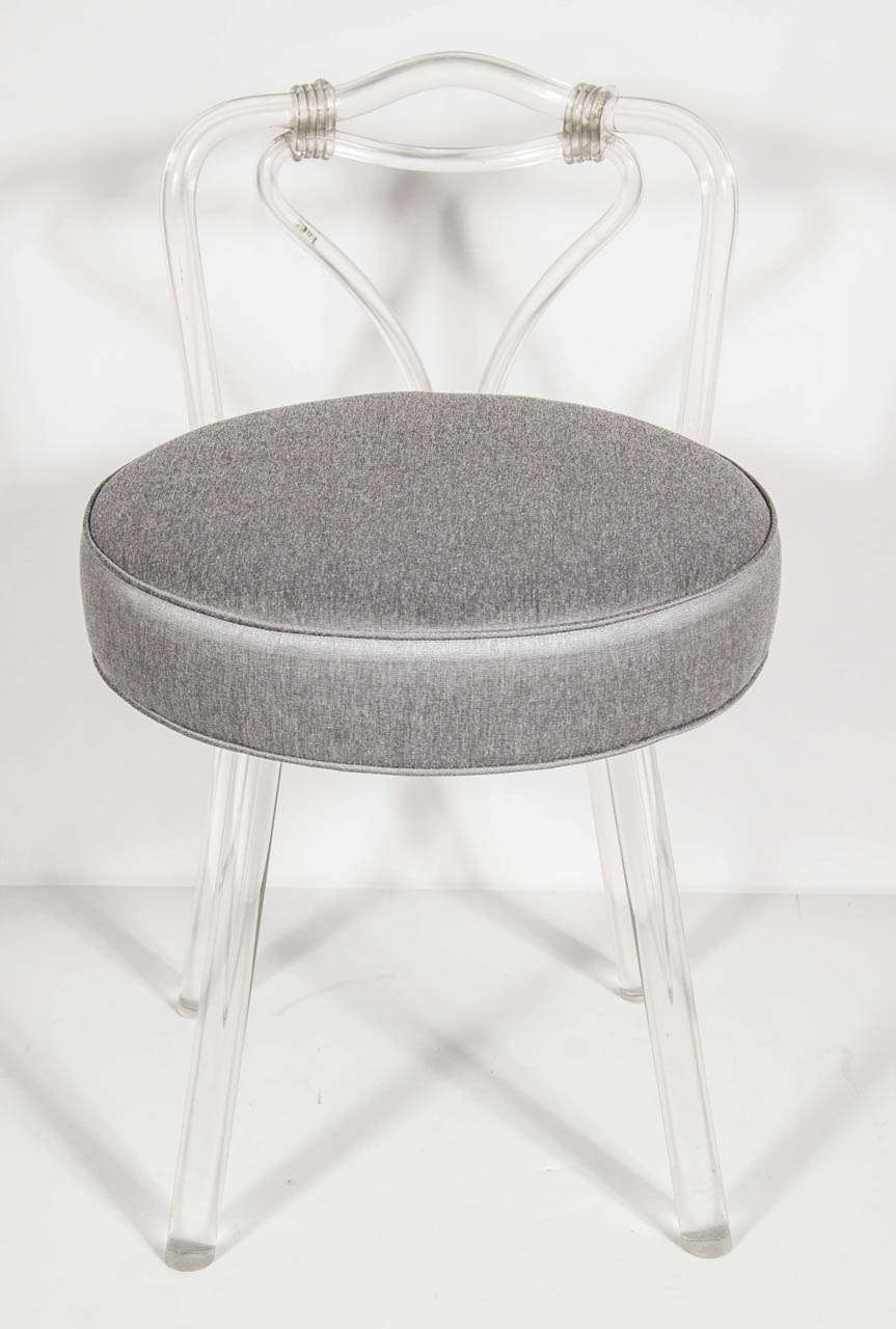 This swivel vanity stool has been newly upholstered in a platinum sharkskin fabric. It features a splayed lucite leg design .