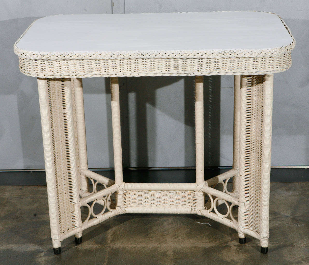 This wonderful table has all of the design and construction details of a Heywood Wakefield Wicker Table from the 1920's. This white painted wicker piece has eight woven joined legs with metal tipped feet and a wooden top. Wooden circular details are