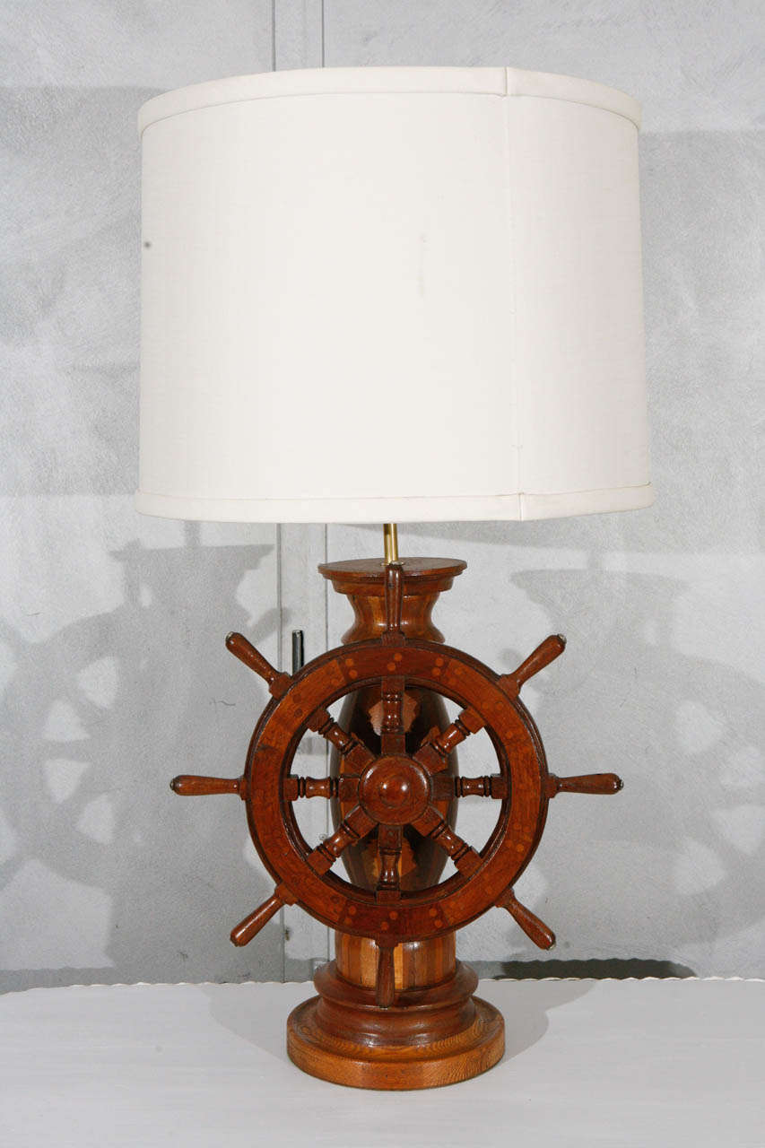 This table lamp is considered to be American, circa 1950's. It has a unique ship's wheel with great shop art inlay details. It has a great proportioned linen lamp shade that adds a crisp modernity to the look. This piece would make a nice lighting