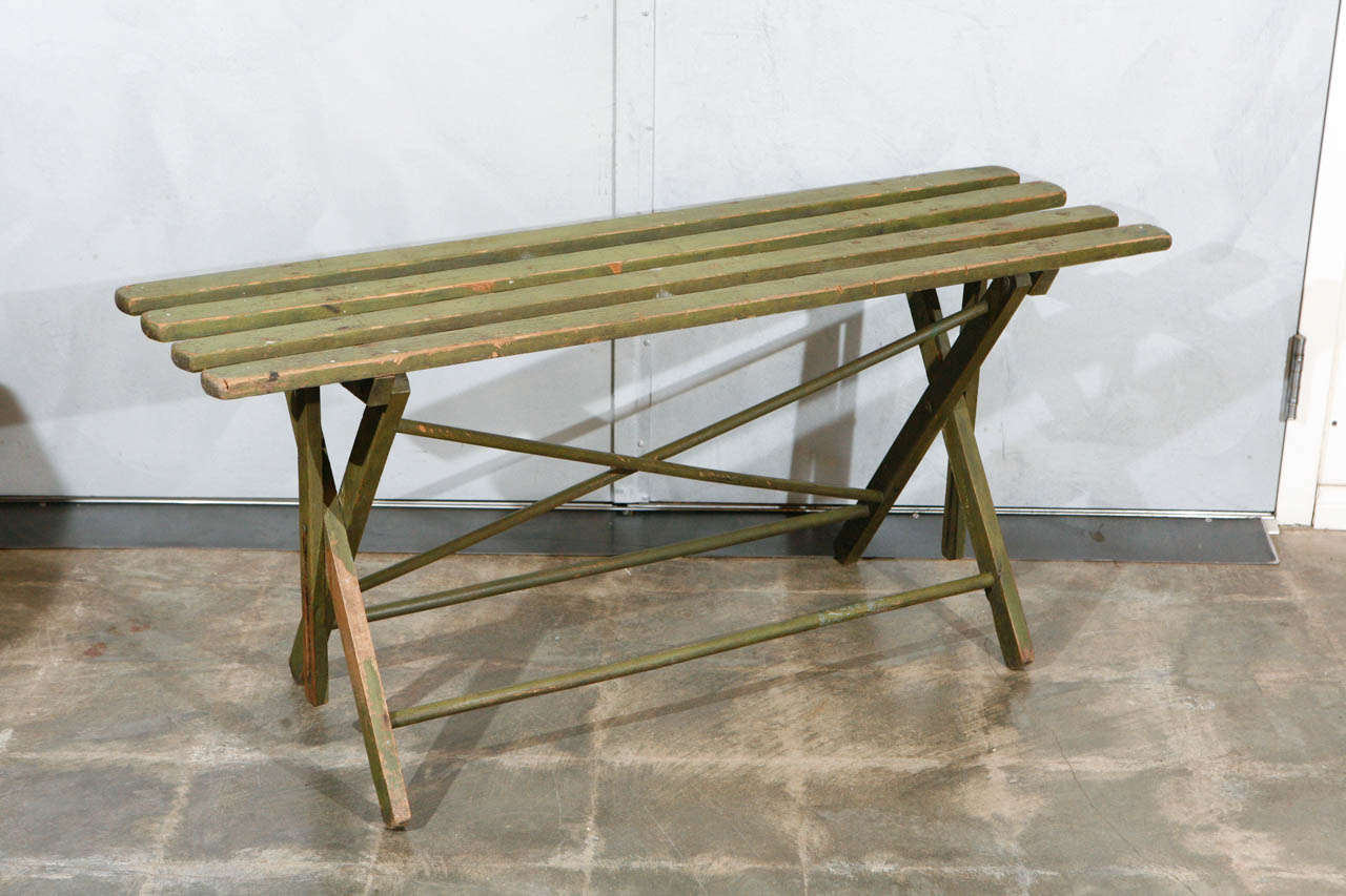 This is an sweet little slated folding garden bench with original light green paint that has a distressed finish. This piece would work well in a variety of settings and can also be utilized as a table for display of decorative items.