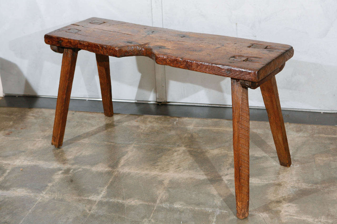 An American primitive, rustic bench, with hand hewed, splayed legs constructed with through mortise and tenon techniques. There is an interesting indent in the center of the bench which could have been carved out to accommodate a specific tool and