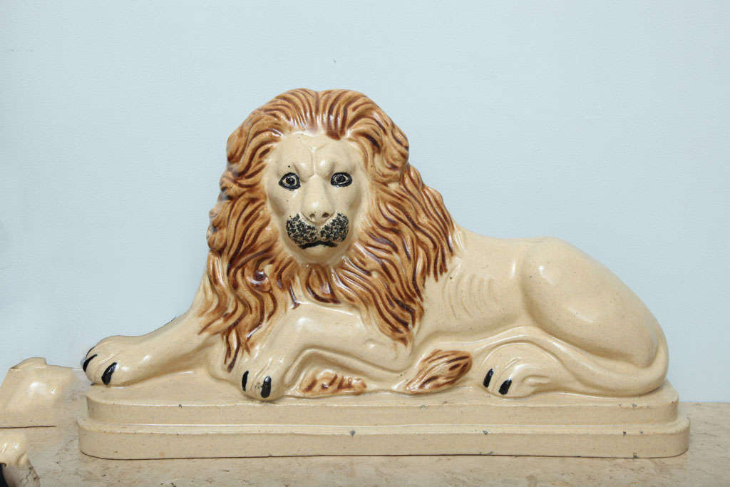 English 19th century glazed earthenware lion with glazed mane, eyes, whiskers and claws on cream colored body, the recumbent beast on double solce plinth.  Unmarked.