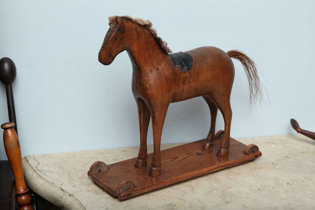 Sculptural Swedish 19th Century carved pine child's pull toy in the form of a horse, retaining its mane and leather saddles on original platform base retaining its wheels, the whole with lovely color and graphic form.