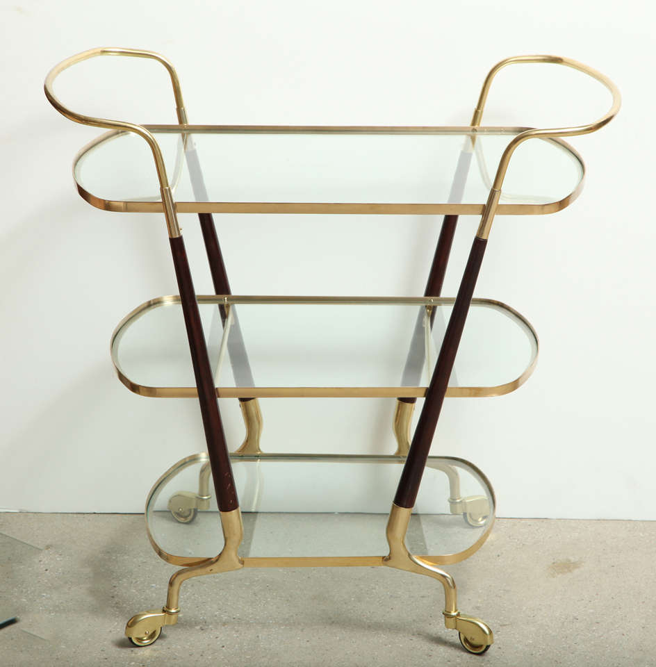 An Mid-Century Italian two handled three tier brass bar cart consisting of 
descending rectangular shelves with curved ends with walnut supports ending with four brass wheels, the brass professionally polished the wood refinished.

Keywords