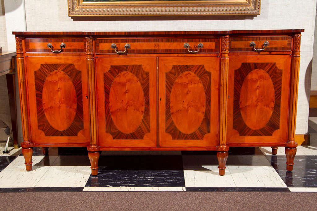 This custom sideboard in English yew wood has a stately appearance augmented by turned and fluted column supports and rosewood inlays and crossbanding. The shape of the top is, with its semicircular corner treatments, enhanced by the multiple