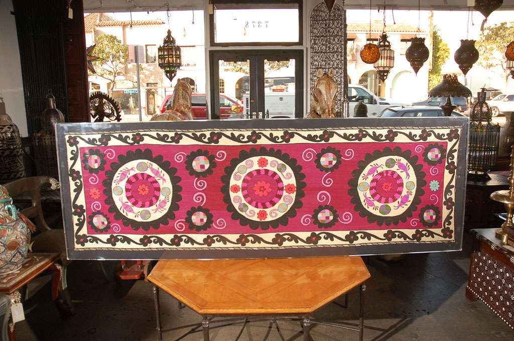 Embroidered Uzbek Suzani framed in a lucite box.
Beautiful suzani hand-stitched Turkish designs with silk in traditional patterns and vibrant pink, fuschia black and ivory colors.
The suzani features a row of three medallions flowers within an