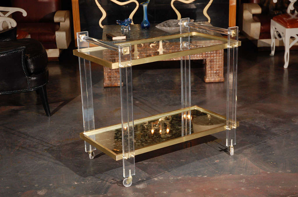 A mid century Lucite and brass tea cart attributed to Karl Springer. Top level is clear glass. Bottom level is antiqued mirror.