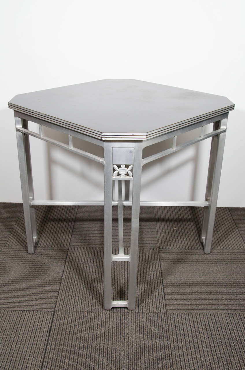 An Art Deco cafe table with bakelite laminate top, black enamel and aluminum speed band trim, and an aluminum modernist cage base accented with abstract foliage, circa 1930s.

Good vintage condition with age appropriate patina. A few scratches.