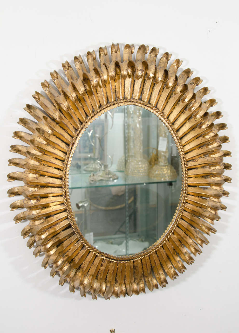 A vintage oval-shaped gilt metal wall mirror with two layers or tiers of curved leaves or petals.

Good vintage condition with age appropriate wear and patina.