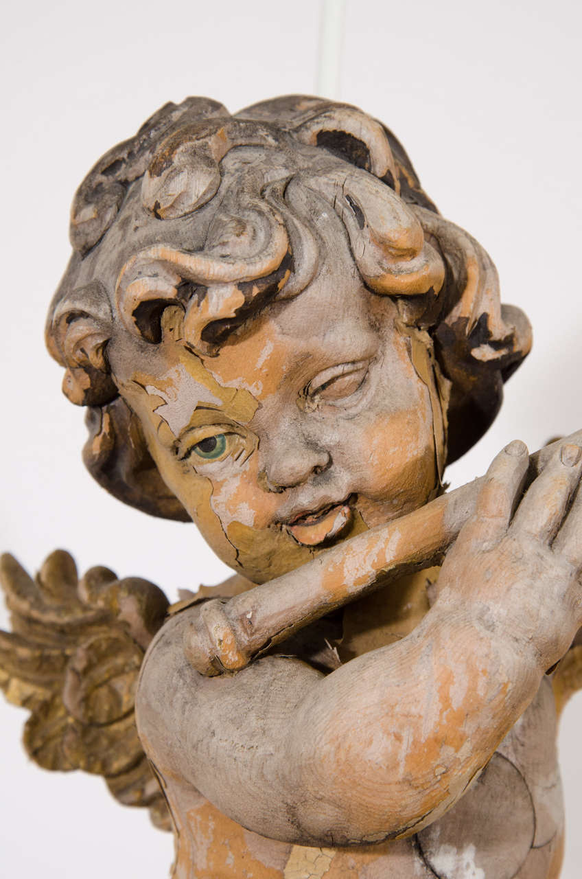 An antique, carved wood musical putto, produced in the 19th century; this beautifully detailed putto, otherwise known as a cherub, depicted playing the flute in midflight, was likely used to decorate a church or sacred space. Fair antique condition,