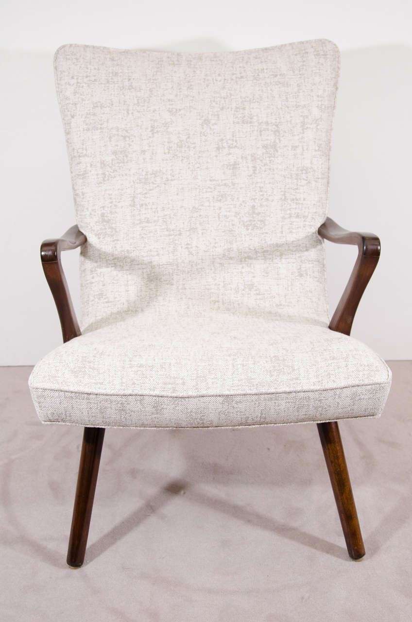 A Scandinavian Modern pair of high backed, winged armchairs with deep seats and dramatically curved wood arms and cylindrical legs. Newly reupholstered in an oatmeal colored fabric. Good vintage condition with age appropriate wear, as well as a few
