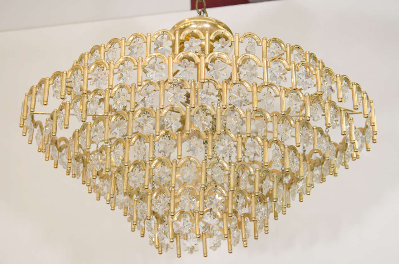 A vintage 1950s multi-tier chandelier, with Austrian snowflake shaped glass crystals. This chandelier takes 10 candelabra base bulbs. Good vintage condition with age appropriate wear. The plastic sleeves on the sockets need to be replaced.  Some are