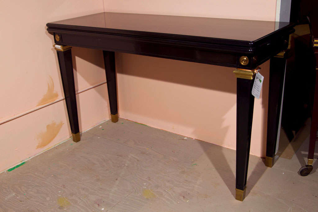 French Directoire style ebonized flip-top console table, circa 1940s, the rectangular top over a narrow frieze decorated with brass mounts, raised on squared tapering legs ending in brass feet. By Jansen.
