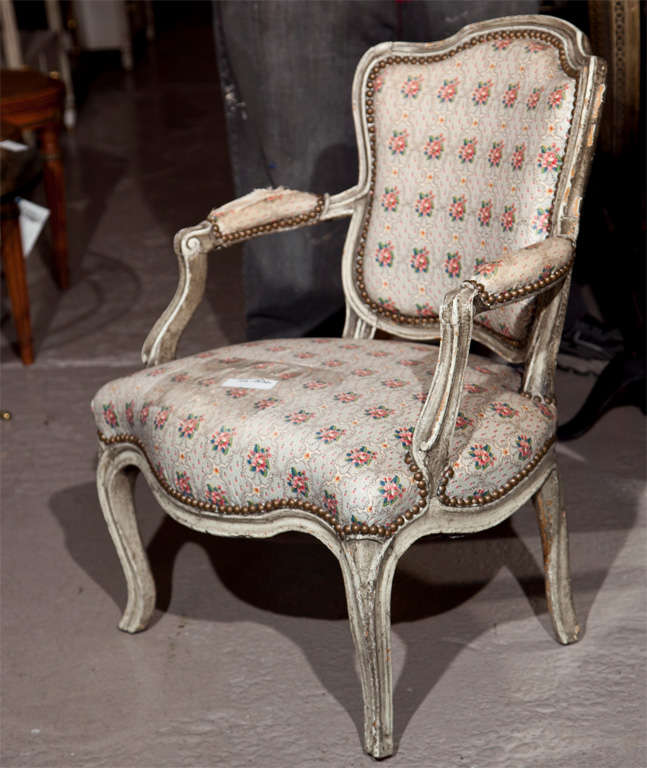 A chic French, Louis XIV style fauteuil, circa 1940s, distress painted frame with padded back and armrests, floral fabric (poor condition) with nailhead decoration, raised on cabriole legs. By Jansen.