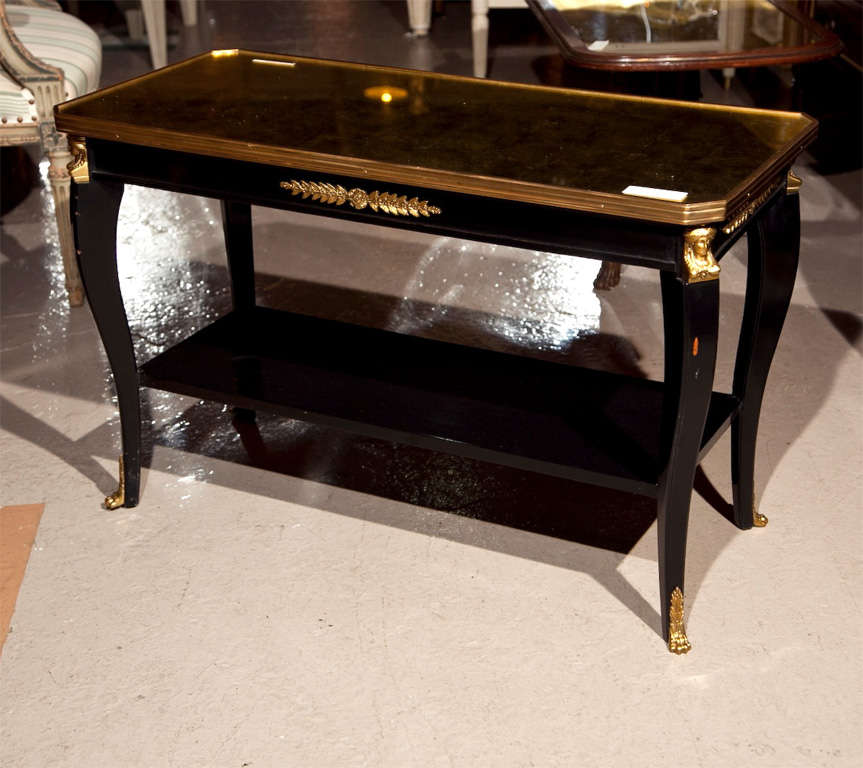 French Empire style coffee table, circa 1960s, the gilt-glass top with bronze banding over a narrow frieze decorated with bronze mounts, raised on cabriole legs headed by bronze figural, joint by a rectangular lower tier, ending in bronze sabots. By