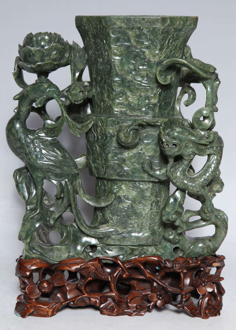 This Intricately Crafted antique Spinach Jade vase has a Phoenix bird, representing Immortality and a Dragon, representing power, surrounding the Flaming Pearl of Knowledge. It rests on a highly polished and equally finely carved Conforming stand. 