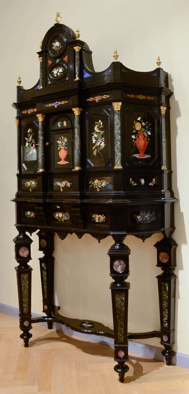 Florentine 19th Century ebony, marble and hard stones marquetry cabinet Three doors and nine drawers. The large drawer opens as a writing desk. Columns, pilasters at the base and capitals in gilded bronze. On the front five marble marquetry panels.
