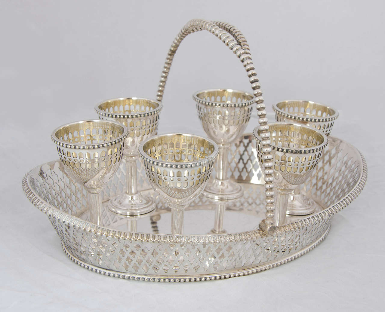 Oval Silver-Plate Basket in openwork design with gently splayed sides, the six egg cups with matching decoration, completed by six elegant spoons.