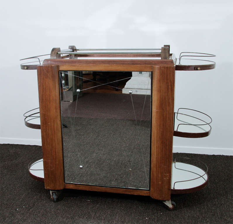 A unique vintage bar cart with rounded Art Deco lines features a central revolving door for storage of bottles and glassware.  The cart is equipped with wheels for ease of movement. Mirrored shelves and brass fittings add interest.