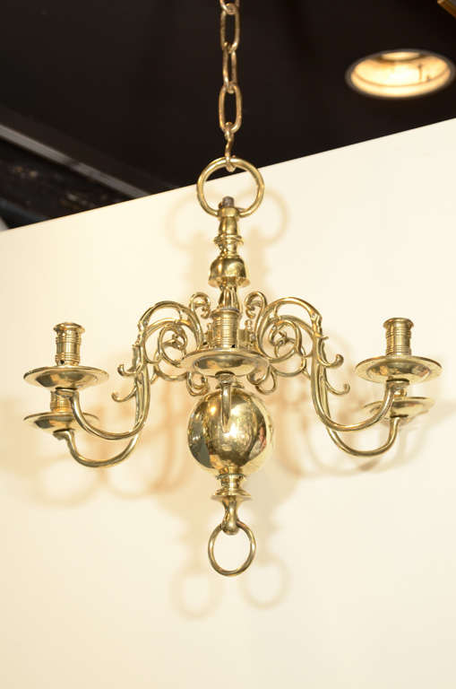 A charming small 19th century Dutch brass six-arm chandelier with scrolling mounted branches emanating from a knopped column terminating in a large ball and ring.
Deeply curved arms hold the candles at a level near the chandelier's body.
  