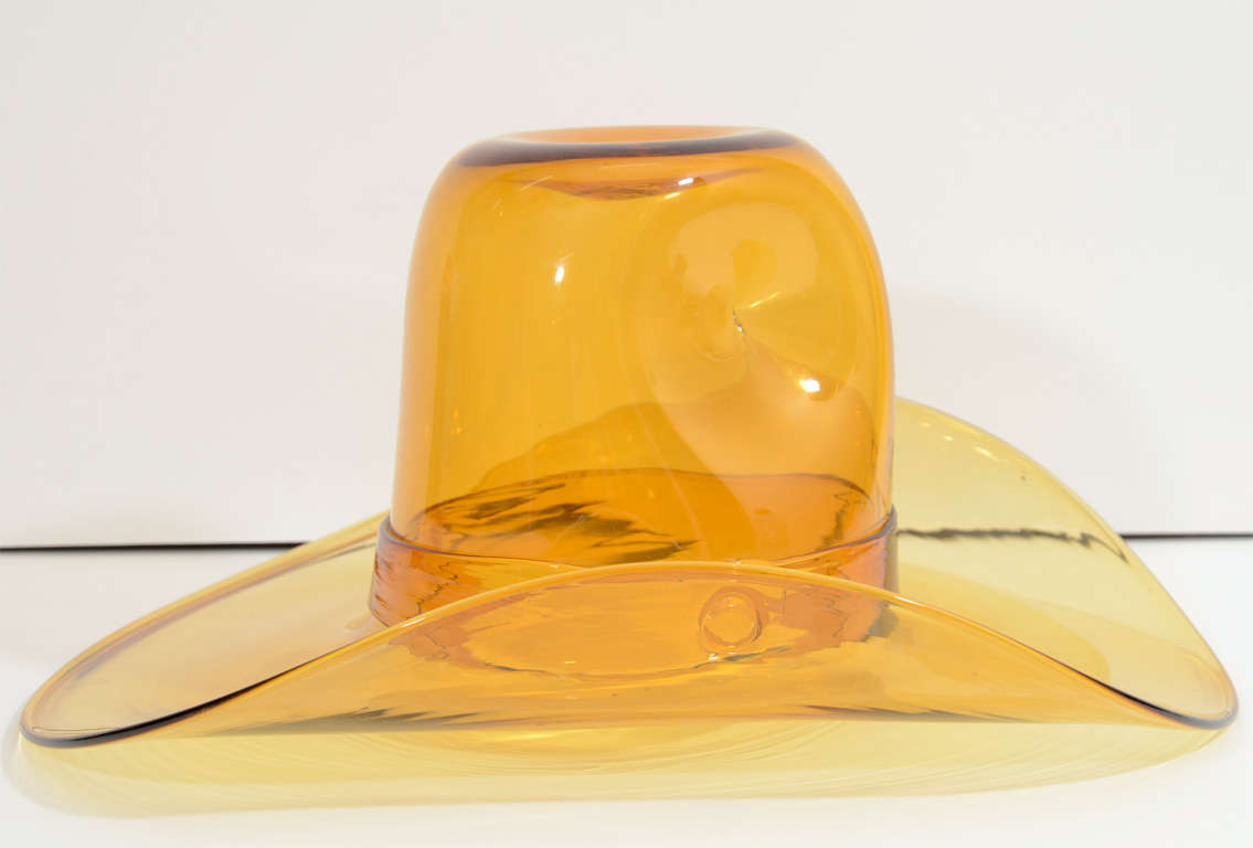 A vintage western style broad brimmed hat in amber glass. The piece may function decoratively or be used as an ice bucket. It retains its Blenko label.