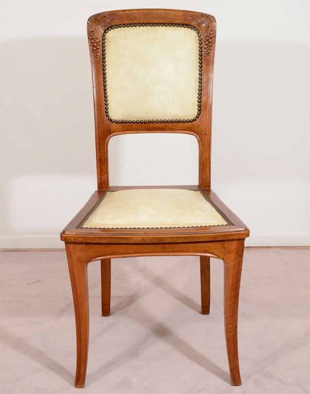 A vintage art nouveau side chair with cream leather upholstery trimmed with brass nail heads and a wood frame with leaf and grape motif. The piece is attributed to Louis Majorelle. It is in vintage condition with age appropriate wear; the leather