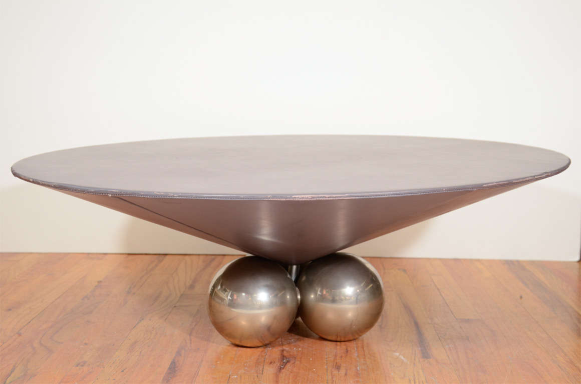 A vintage coffee or cocktail table with a surface wrapped in chocolate colored leather and base composed of three silvered bronze globes. 

The piece is in good vintage condition with age appropriate wear; some scratching and wear to leather.
