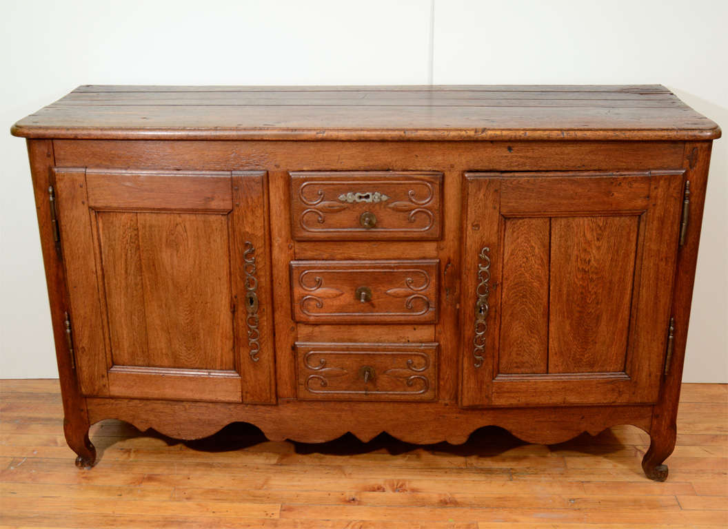 An antique oak buffet from France with three central drawers flanked by two cabinets. The piece has curving legs and a scalloped skirt. The piece is in antique condition with some age splits in the wood.