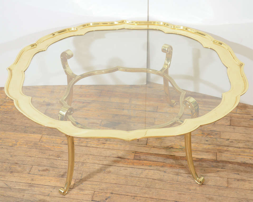A vintage Hollywood Regency glass top coffee table with a scalloped and scrolling frame and base in polished brass; glass surface is removable. Good vintage condition with age appropriate wear; some scratching/scuffs to brass and glass.