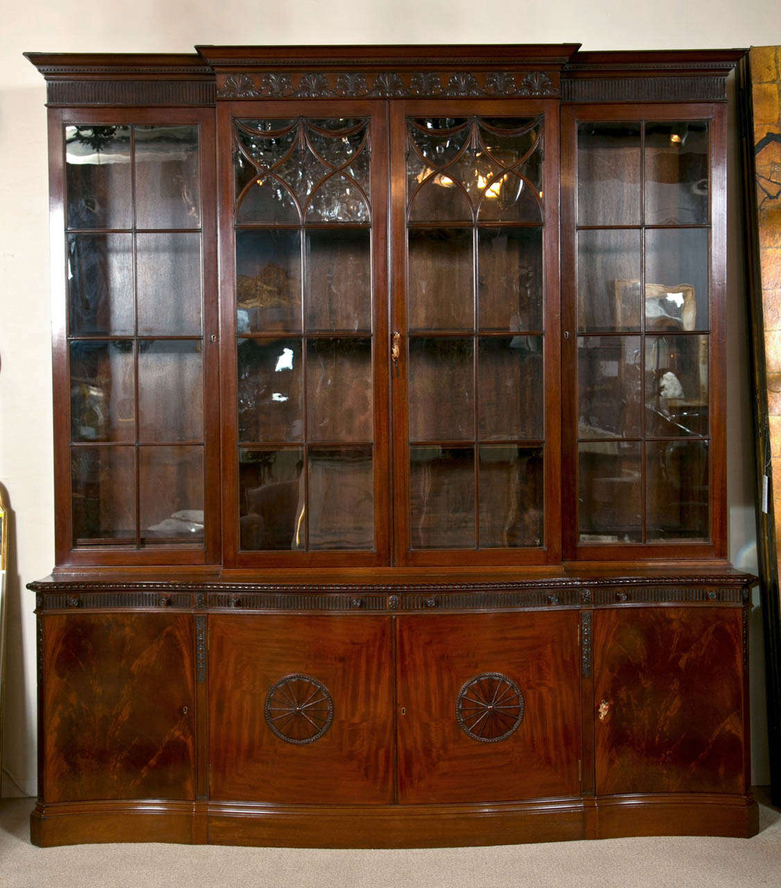 A very finely carved mahogany breakfront bookcase with mitered doors having swag mullions set atop a low hip base. The bookcase has personal reading slides for four made by Maple & Co which was the premier furniture maker in London and Paris during