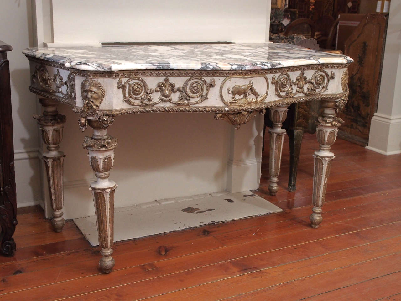 A large, marble-top console table, the serpentine marble top above a frieze with elaborate rinceau flanking a cartouche, on muscular, tapered legs 