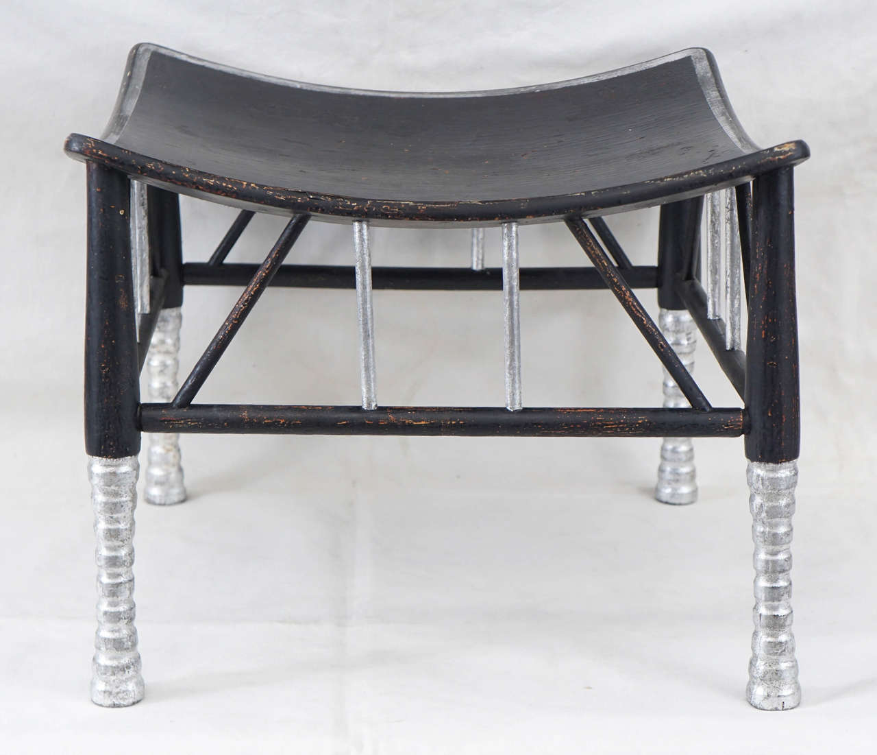 This stool made by Liberty & Company is most likely from the early part of the 20th century. Once in wood tones the stool was redecorated and comes soon after the discovery of Tutankhamun's Tomb by Howard Carter. The black and silver decoration is