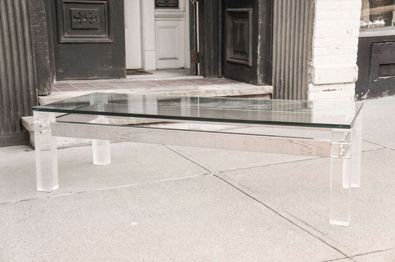 This hip and cool coffee table is made from heavy square stock lucite legs connected with chromed metal structural supports and is topped by a thick glass top. Made in the 70's and used in a house interior done circa 1975  which has  remained intact