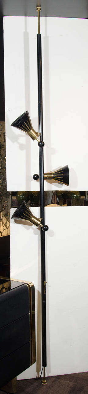 Ultra modernist floor lamp with lengthened pole design and tension rods at either end. The lamp has a sophisticated form and is designed to hold itself between the floor and ceiling. Constructed in metal with a black enameled finish, and has brass