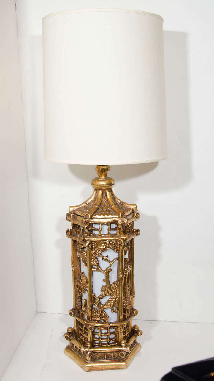 Pair of exceptional and exquisite lamps in hand carved resin and wood with hand applied 24k gold leaf finish. The lamps have a sophisticated pagoda design with Asian scenery and landscape motifs. Shown with custom tall drum shades in an off-white