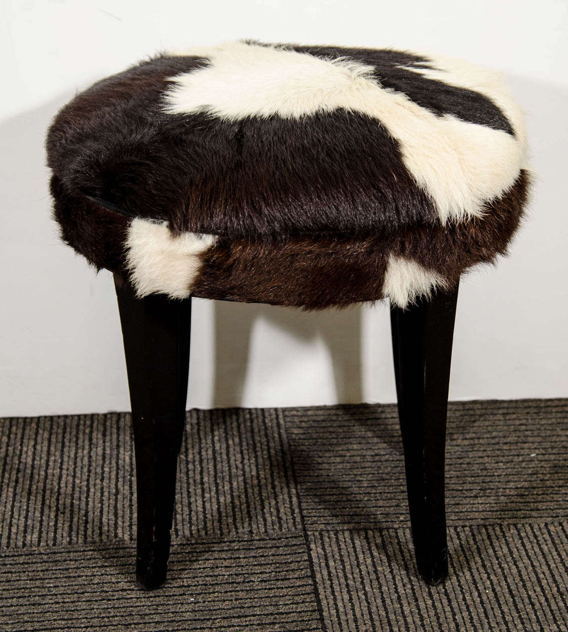 A vintage stool with black and white cow hide upholstery and ebonized legs. 

The stool is in good vintage condition with faint scratches and nicks on legs.