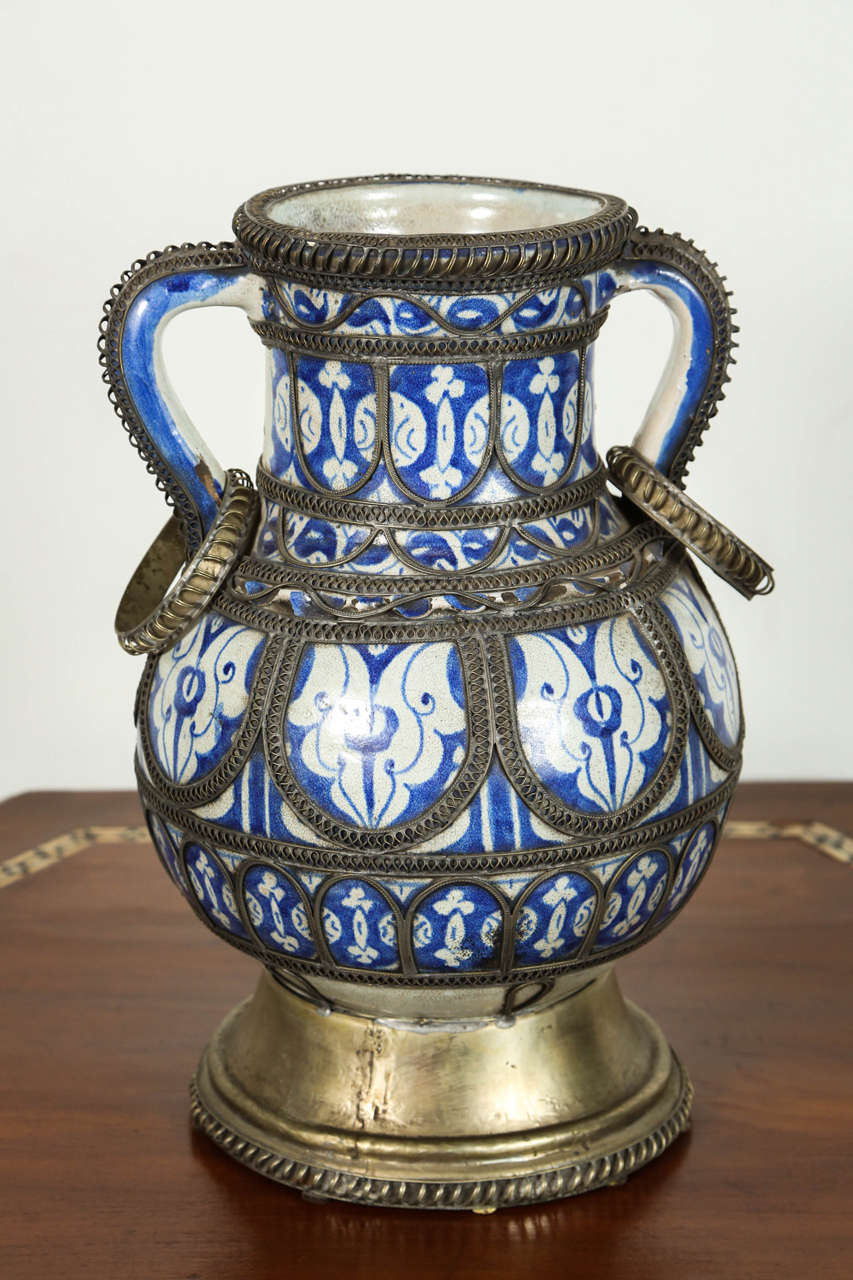 Ancien vase marocain bleu et blanc sur pied en céramique de Fès. 
Vase de style mauresque fabriqué à la main et orné d'un fin travail filigrane en argent nickelé:: avec deux poignées. 
Ancien motif hispano-moresque sur urne en céramique bleu de Fez.