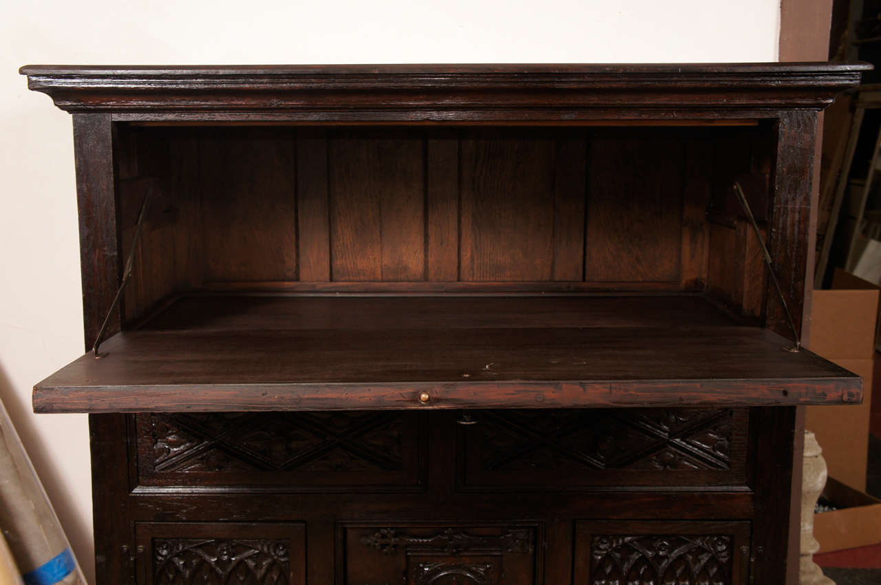 Hand-carved paneled Jacobean-style abbatant or secretaire with drop-down leaf for a writing surface and storage space.  Two drawers below and three-door cabinet at the bottom.  Decorative paneling on front and linen-fold paneling on the sides could