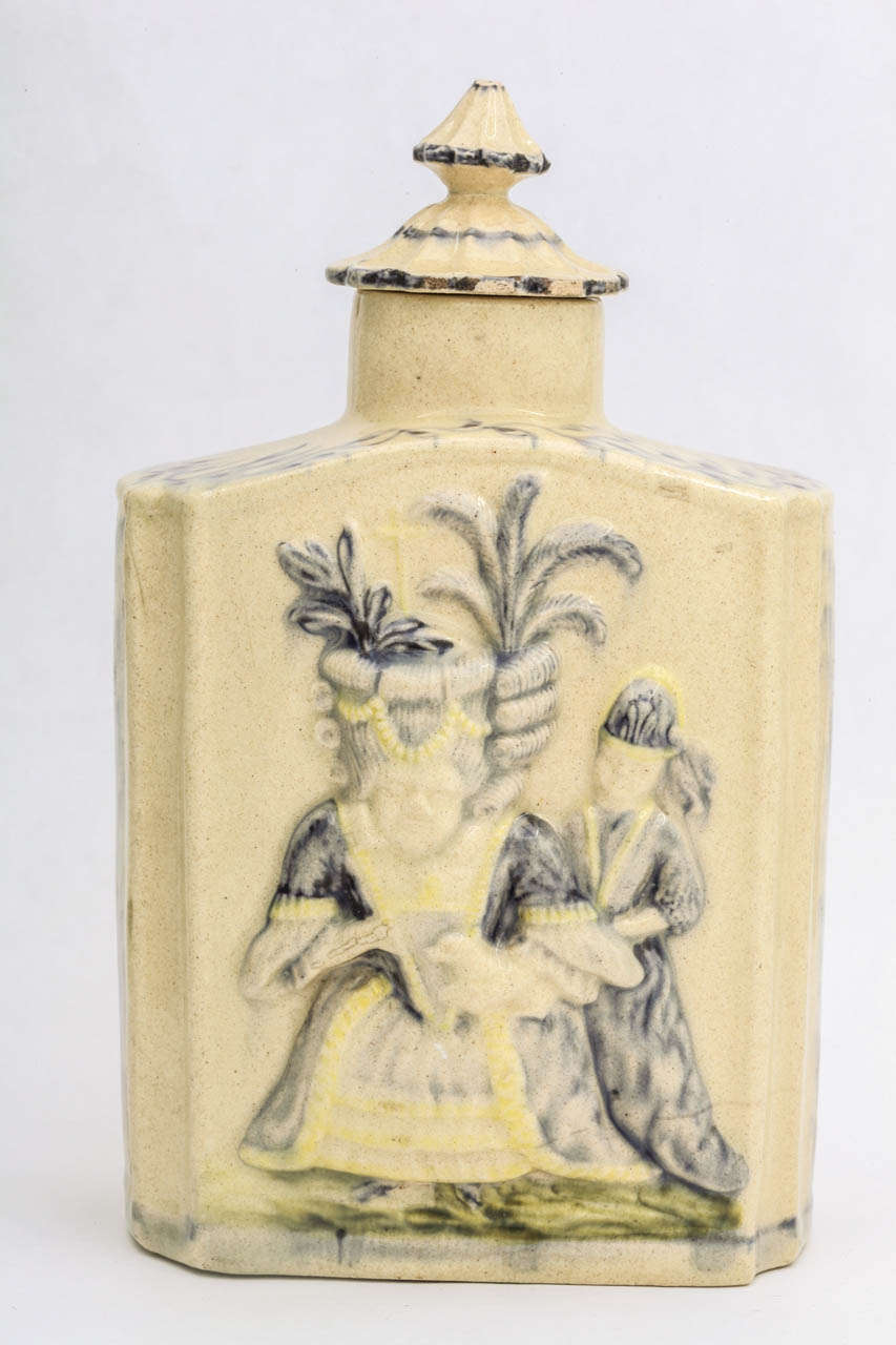 A fine English creamware pottery covered tea caddy molded in relief with Macaroni figures, decorated in underglaze blue and green colors