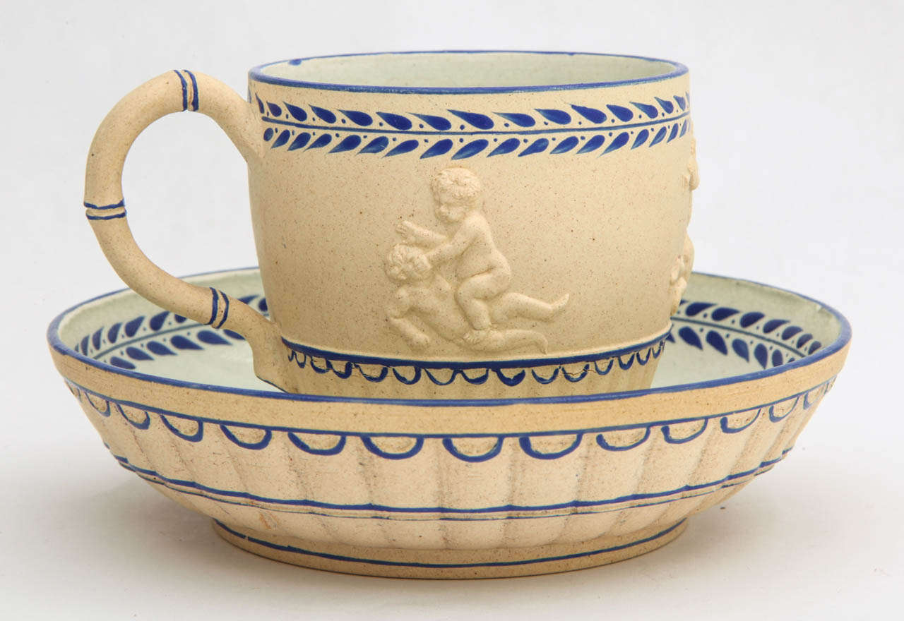 A rare Wedgwood enameled caneware cup and saucer decorated with Bacchanalian Boys at Play, blue and white enamel, upper-lower case mark