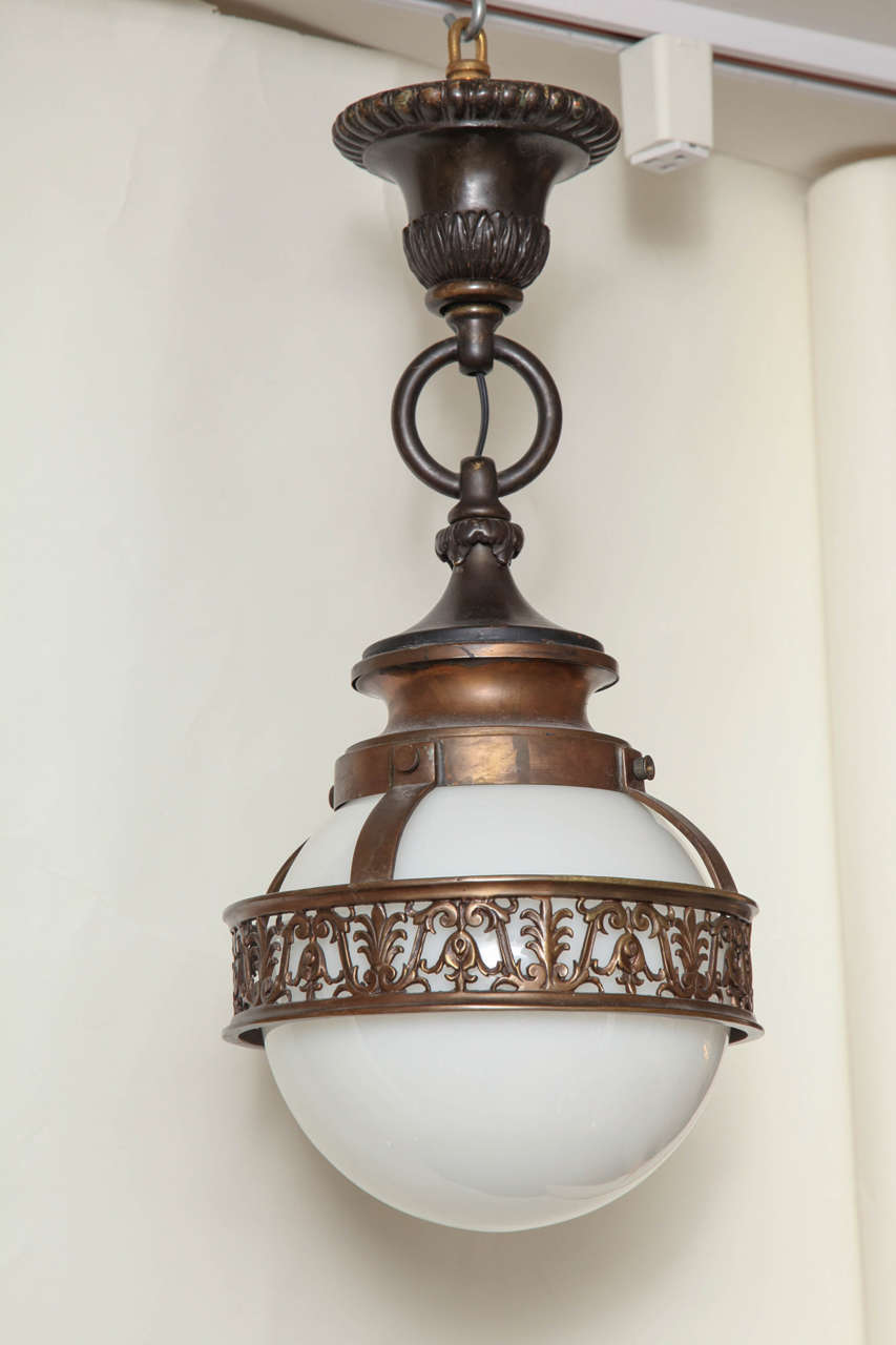 A Beaux Arts bronze ceiling fixture , the fixture's white opaline glass ball shaped dome having an open fret frieze with neoclassical motifs encircling centre attached to fitting with leaf shaped details below ring and canopy.  Attributed to Edward