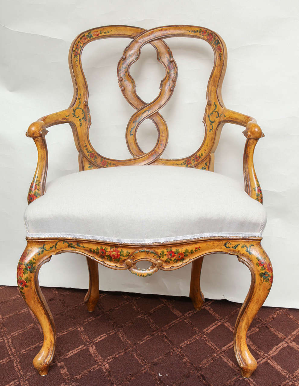 A pair of Italian Rococo style open armchairs, the chair back with arched frame and upholstered seat supported by cabriole legs and pierced carved apron. The frames decorated overall with hand-painted floral motifs on a yellow ground.
