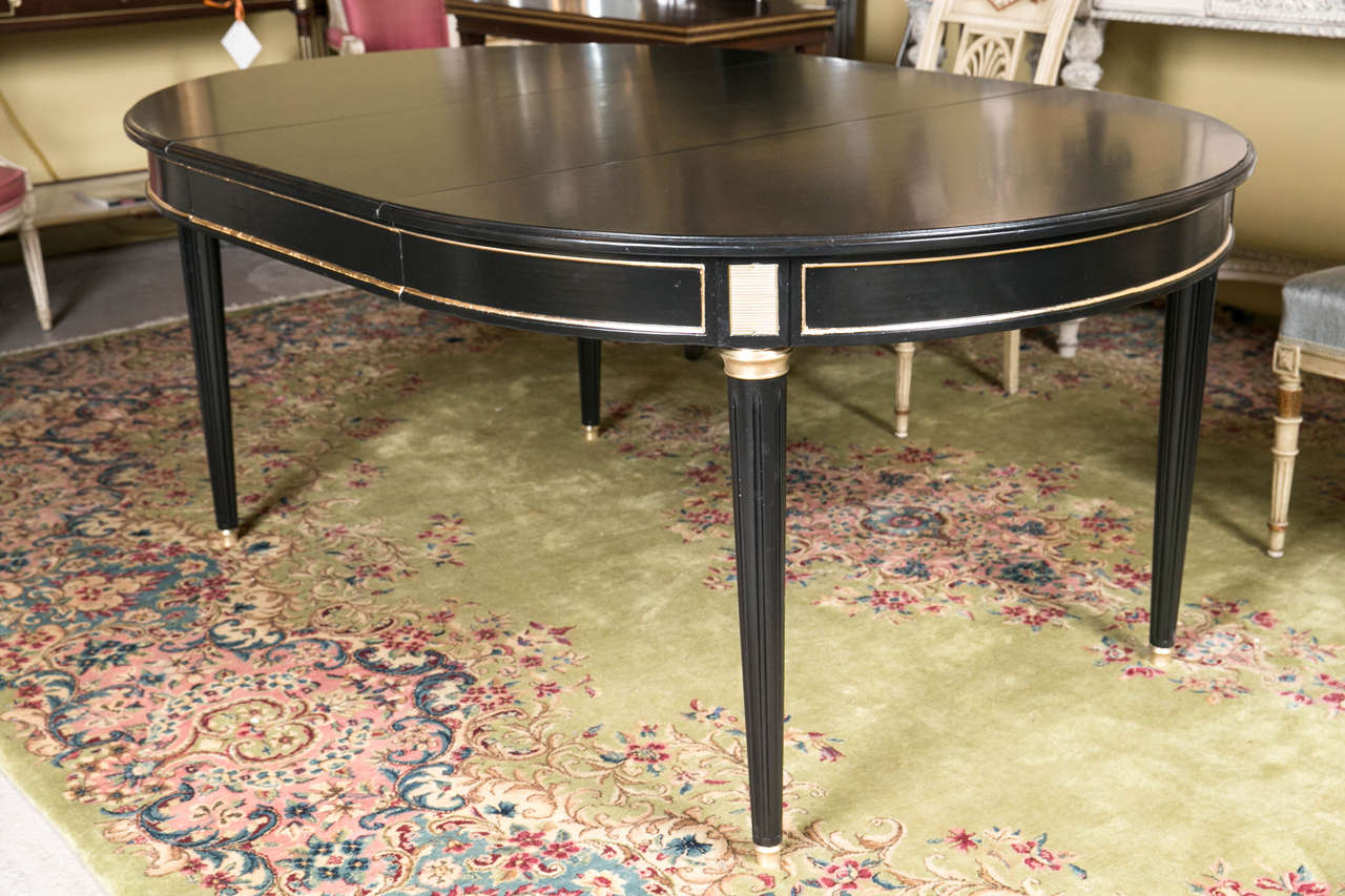A circular Jansen three-leaf ebonized dining table. Fine Louis XVI style dining table by Maison Jansen. The bronze sabots leading to a tapering fluted leg terminating in bronze caps. The bronze framed apron having cookie cutter corners. The top with