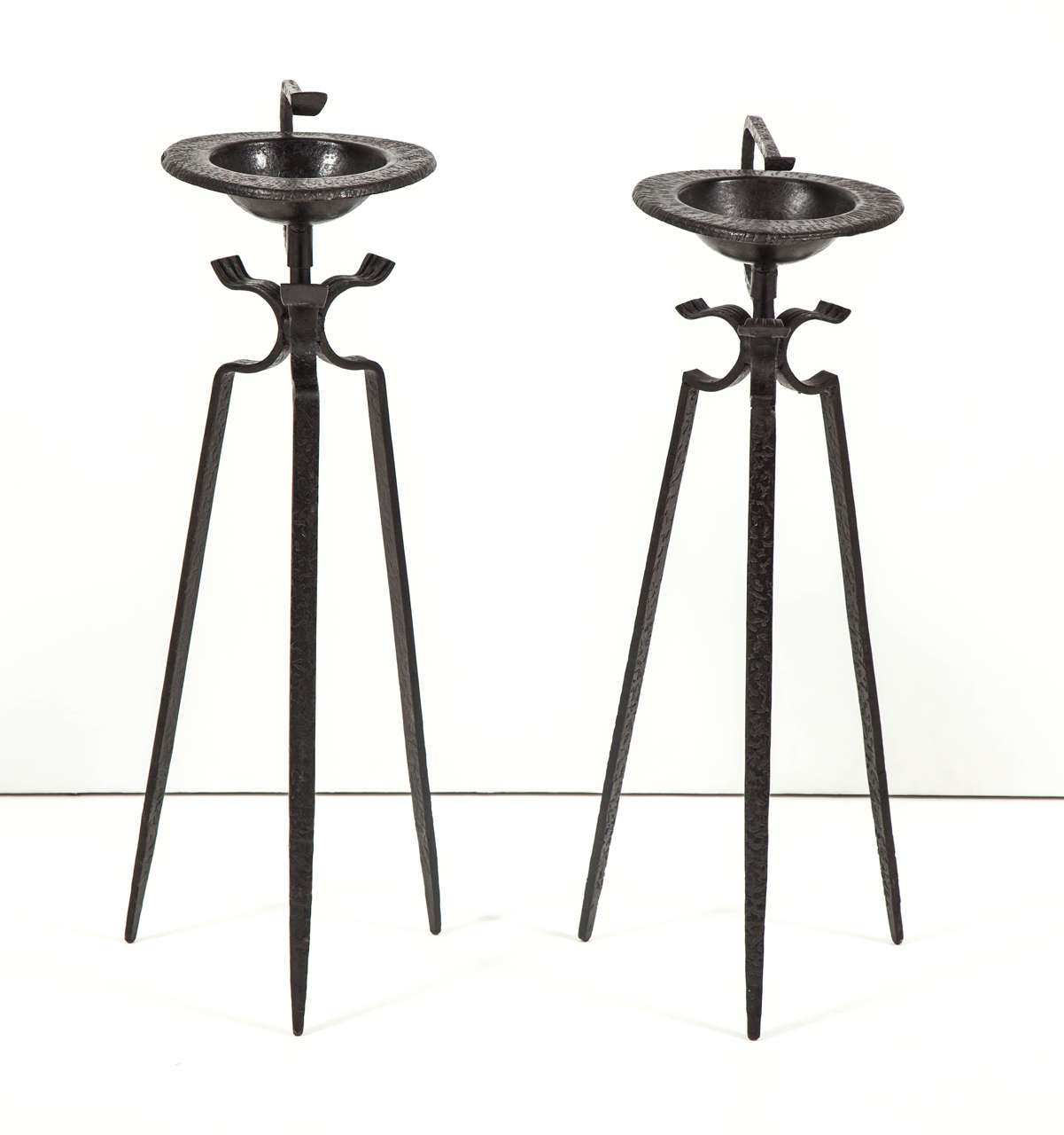 Tripod smoking stands with curling top handles in black hammer-finished iron supporting rounded triangular removable ashtrays, French, circa 1950. Completely handmade and finished, the pair shows some minor differences in design and dimensions.
