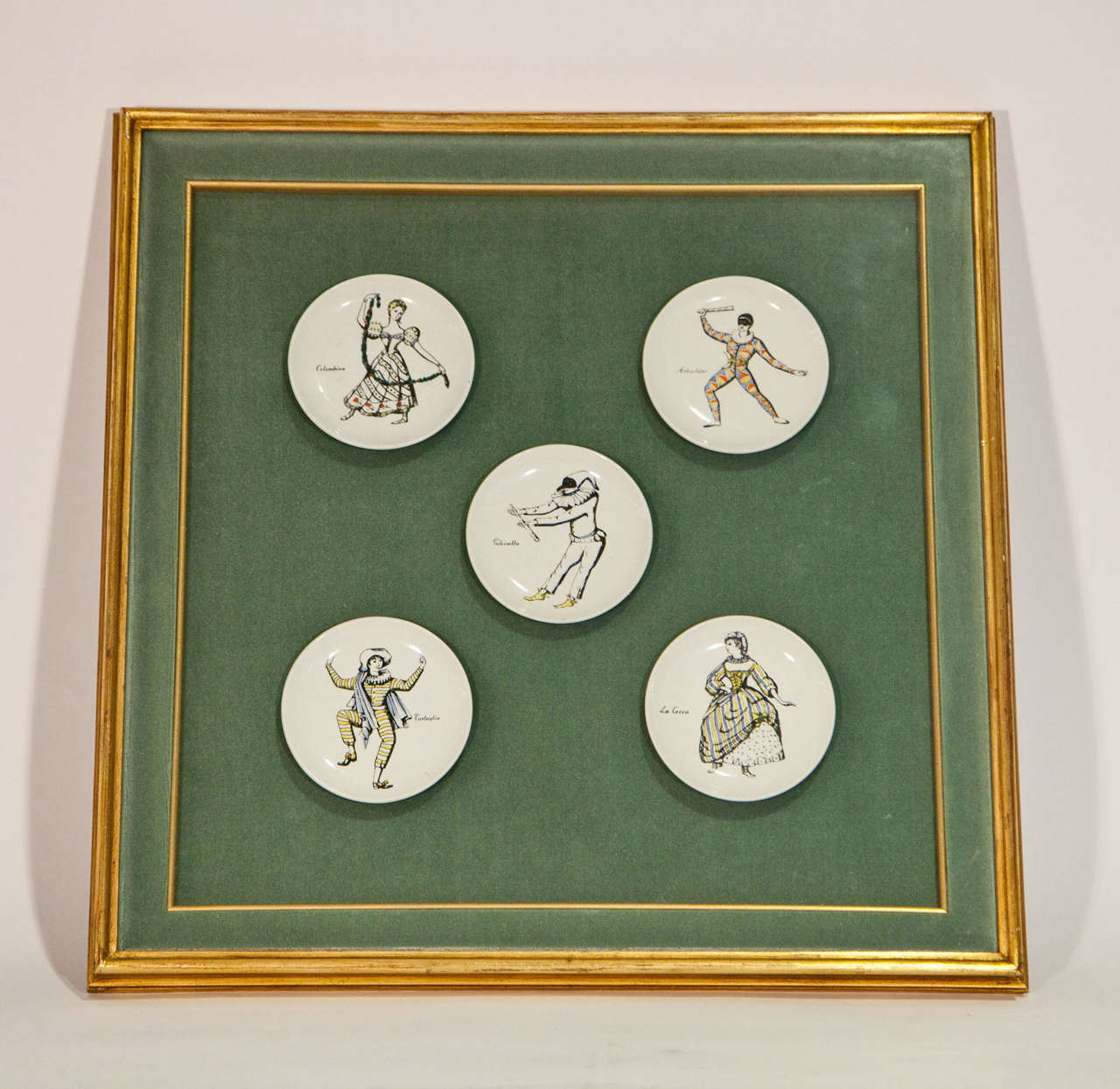 18th century engravings of Commedia dell'Arte actors hand-painted on porcelain plates, framed together in an eau-de-Nile velvet shadowbox with a giltwood frame. The plates are from the series 