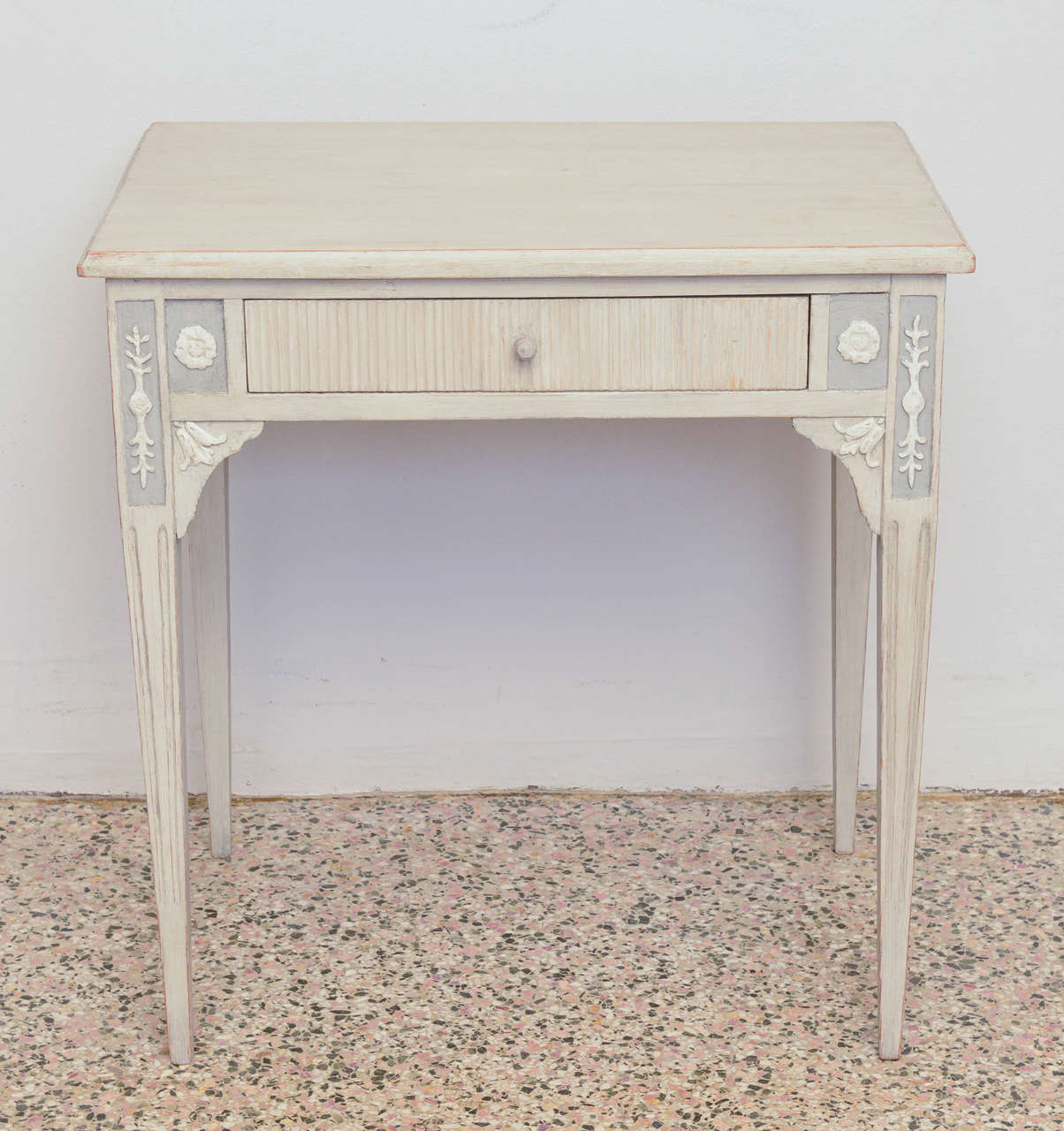 19th century antique Swedish Gustavian table in a greyish washed color with beautiful raised carvings; has center drawer with raised ribbed panel and original wood pull; carvings on either side of the drawer are raised like a cameo and are a floral