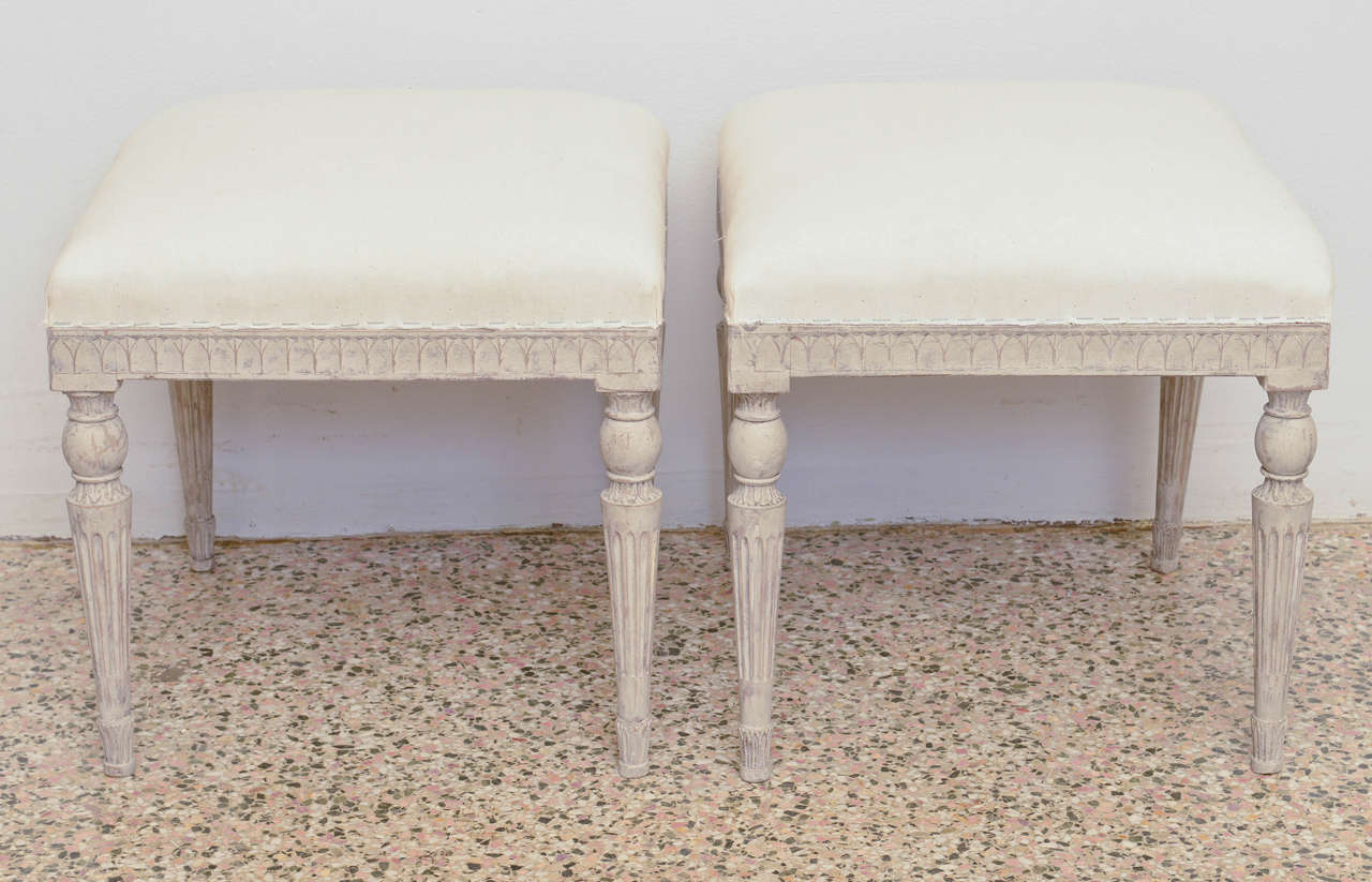 Early 19th century antique Swedish Gustavian stools; with tapered fluted, and carved legs. Seat apron edge is beautifully carved with a leaf like design. Wood is a grayish washed color. Stools are signed below seats: Wallender & Co., Stockholm.