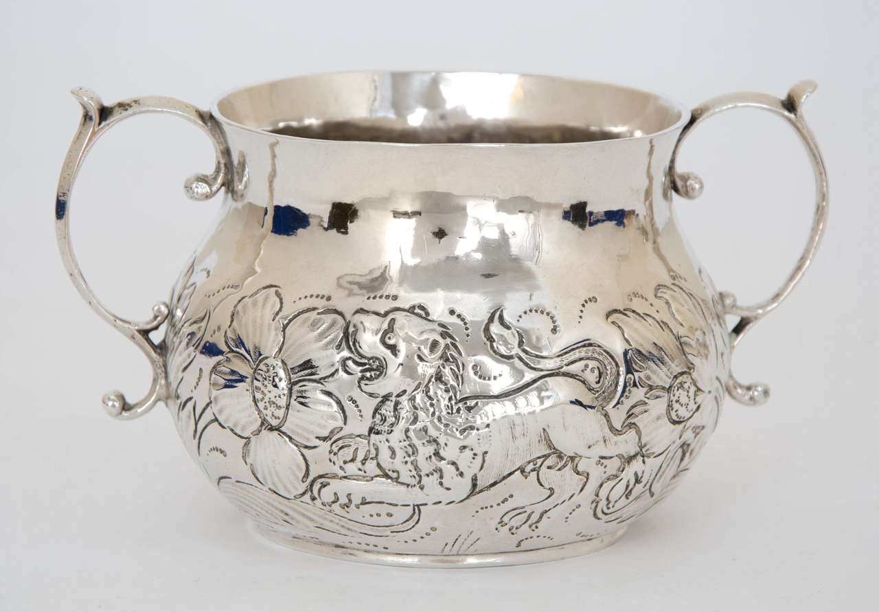 A Charles II silver two-handled porringer,made in 1679, circular bellied form, embossed with a running unicorn and lion within foliate scroll decoration, scroll handles , the base scratch initialled 
